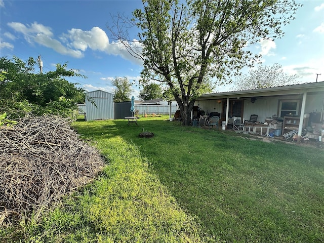 view of yard with a storage unit, an outbuilding, fence, ceiling fan, and a patio
