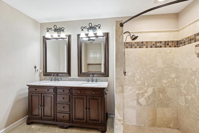 full bathroom with baseboards, a sink, double vanity, and a tile shower