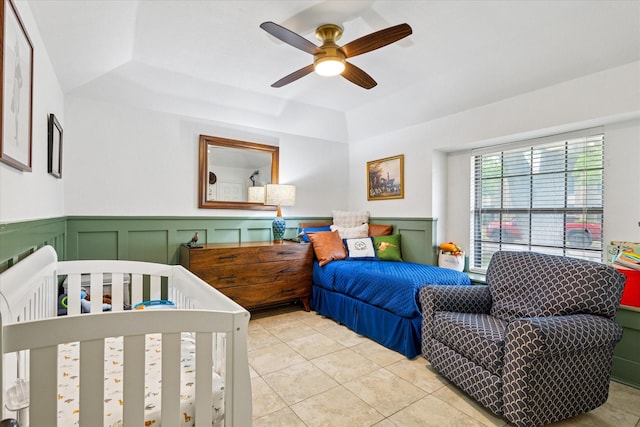 bedroom featuring a decorative wall, a ceiling fan, a wainscoted wall, and tile patterned floors
