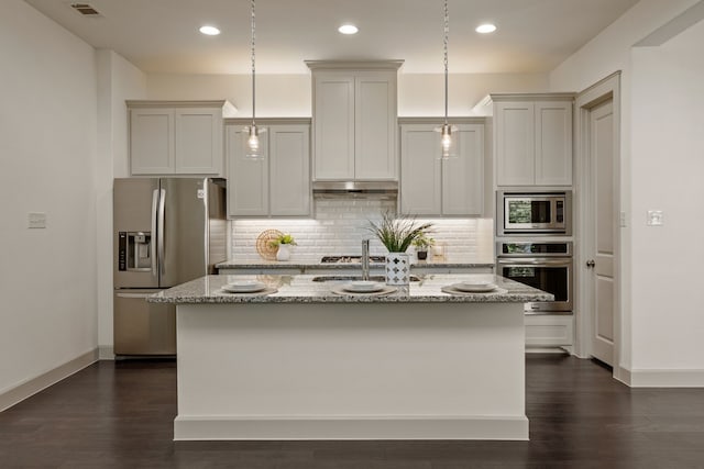 kitchen featuring a sink, backsplash, light stone countertops, an island with sink, and appliances with stainless steel finishes