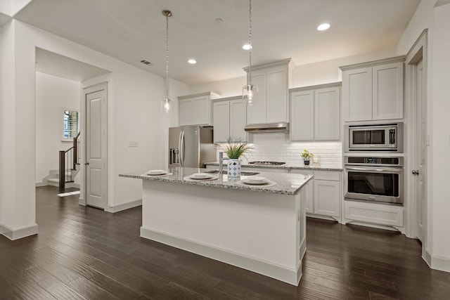 kitchen with stainless steel appliances, under cabinet range hood, decorative backsplash, and dark wood-style flooring
