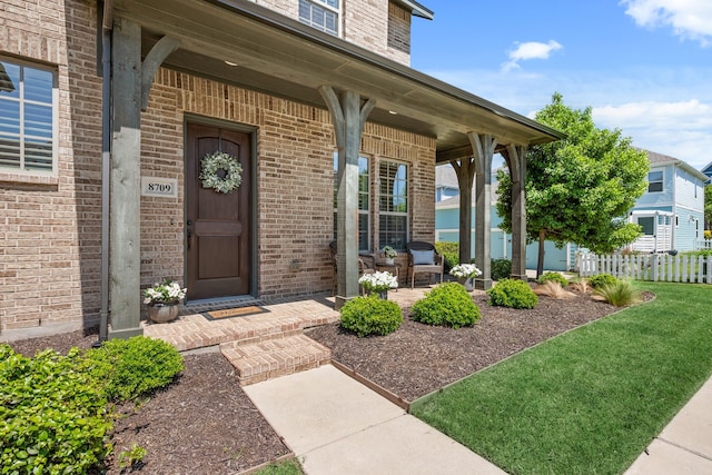 doorway to property featuring brick siding, a porch, and fence