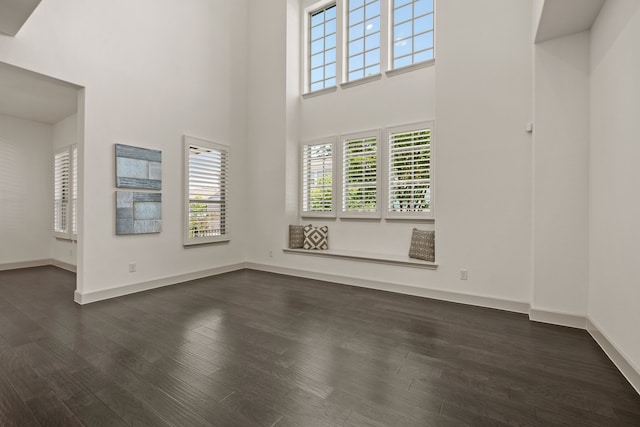 unfurnished living room with dark wood-type flooring, a high ceiling, and baseboards
