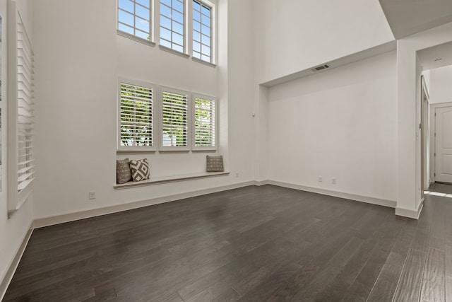 unfurnished living room with baseboards, visible vents, a towering ceiling, and dark wood-style flooring