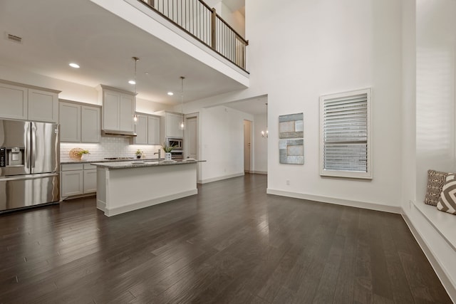 kitchen with decorative backsplash, an island with sink, appliances with stainless steel finishes, dark wood-type flooring, and visible vents