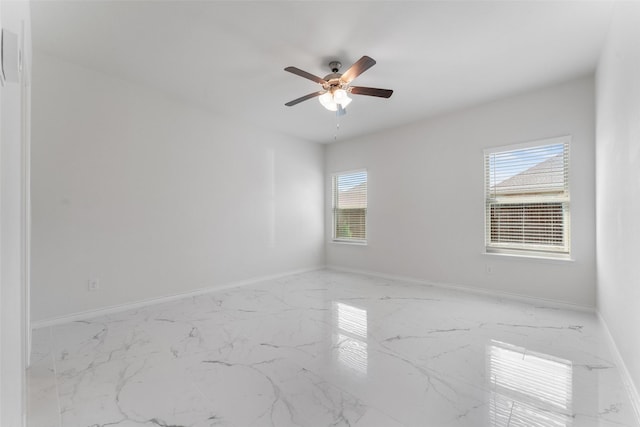 empty room with marble finish floor, baseboards, and a ceiling fan