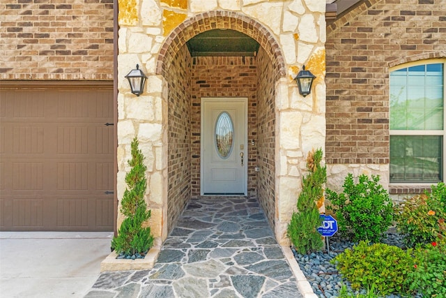 view of exterior entry with brick siding, stone siding, driveway, and a garage