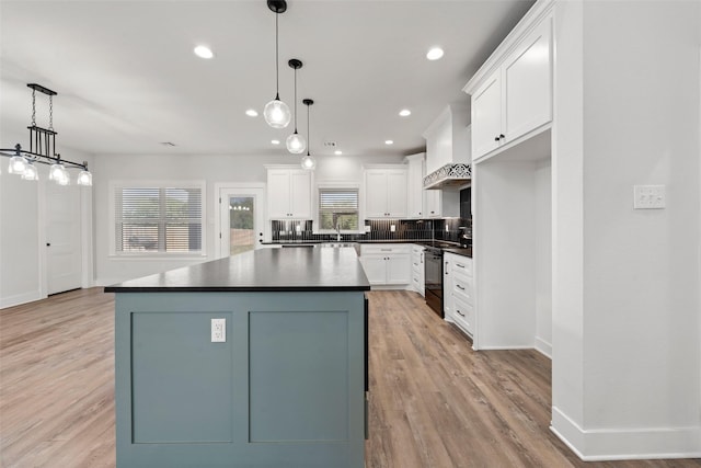 kitchen with wall chimney range hood, dark countertops, a sink, black range with electric cooktop, and white cabinetry
