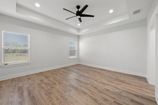 unfurnished room with a tray ceiling, visible vents, baseboards, recessed lighting, and wood finished floors