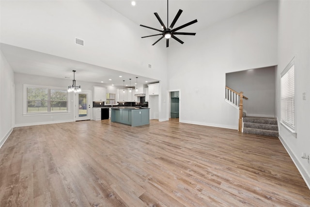unfurnished living room with visible vents, light wood finished floors, baseboards, and ceiling fan with notable chandelier