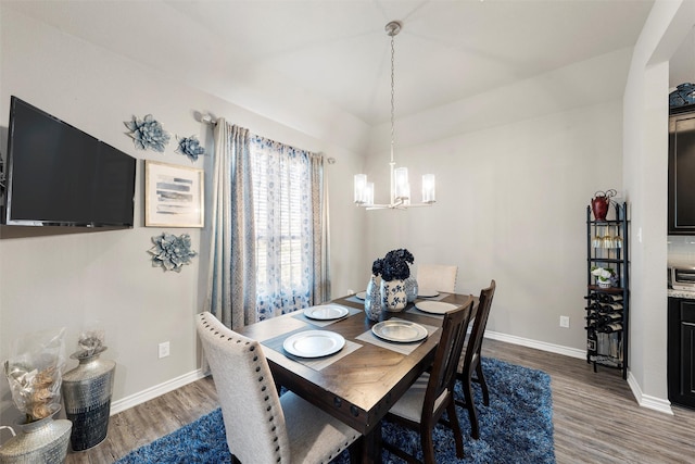 dining space with baseboards, a notable chandelier, wood finished floors, and lofted ceiling