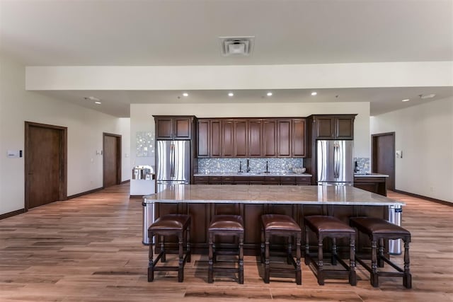 kitchen featuring a kitchen breakfast bar, a large island, stainless steel refrigerator, freestanding refrigerator, and decorative backsplash