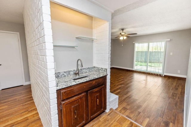 kitchen featuring ceiling fan, light stone counters, light wood-style floors, and a sink
