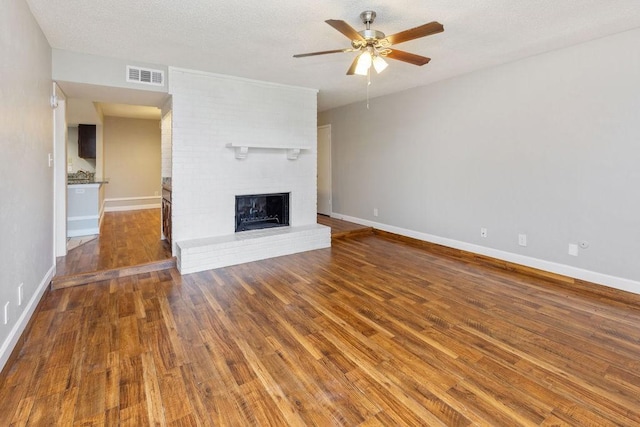 unfurnished living room with baseboards, visible vents, a ceiling fan, wood finished floors, and a fireplace