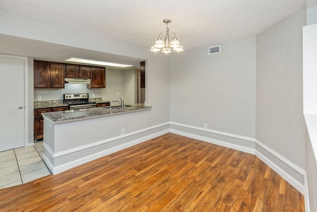 kitchen featuring under cabinet range hood, visible vents, stainless steel electric range, light wood-style flooring, and a notable chandelier