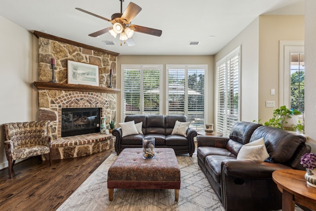 living room featuring ceiling fan, a stone fireplace, wood finished floors, and visible vents