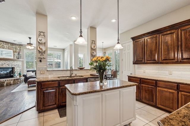 kitchen featuring stone counters, a kitchen island, a ceiling fan, and a sink