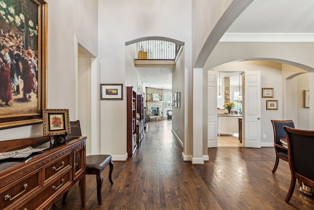 foyer with baseboards, arched walkways, dark wood-type flooring, and ornamental molding