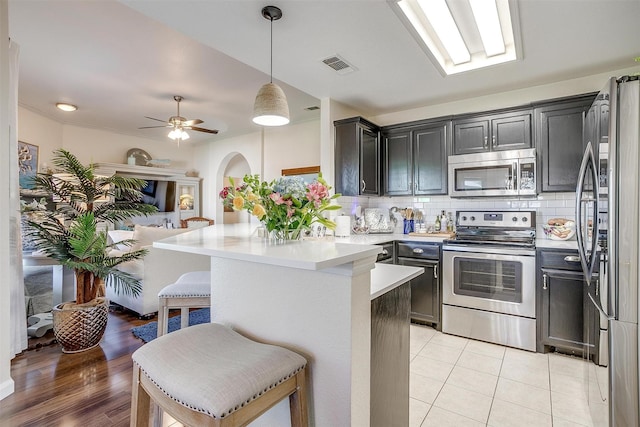 kitchen with a kitchen breakfast bar, stainless steel appliances, light countertops, visible vents, and tasteful backsplash