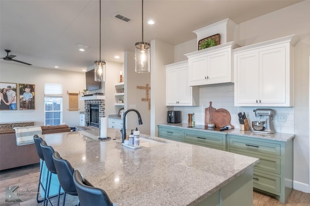 kitchen with a sink, open floor plan, visible vents, backsplash, and white cabinetry