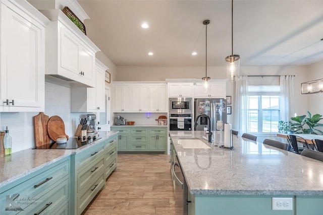 kitchen with stainless steel appliances, a large island with sink, a sink, and white cabinetry