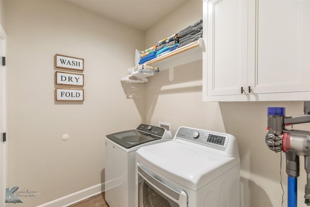 clothes washing area featuring wood finished floors, baseboards, washer and clothes dryer, and cabinet space