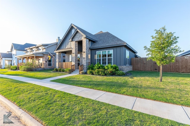 view of front of property featuring a front lawn, board and batten siding, a shingled roof, fence, and brick siding