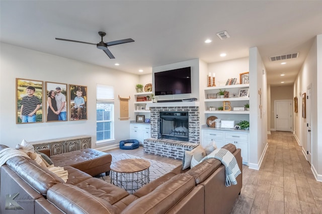living area featuring a ceiling fan, visible vents, light wood-style floors, and a brick fireplace