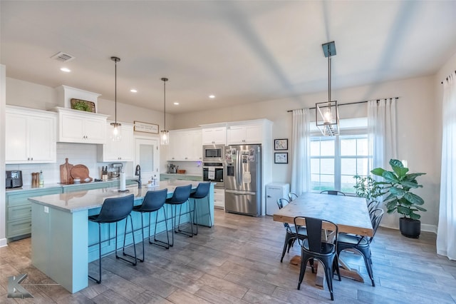 kitchen with white cabinets, a center island with sink, visible vents, backsplash, and appliances with stainless steel finishes
