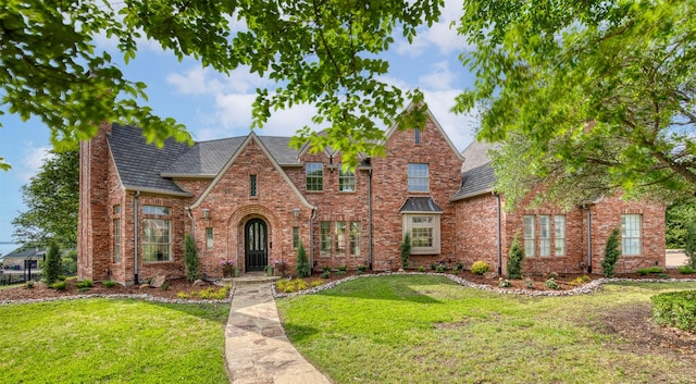tudor home featuring a front yard, a chimney, and brick siding