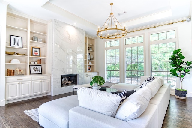 living room featuring a chandelier, a tray ceiling, ornamental molding, dark wood finished floors, and built in features