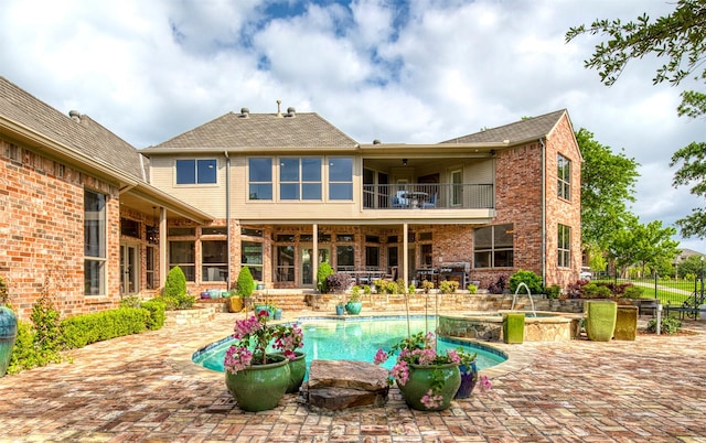 rear view of property with brick siding, an in ground hot tub, a patio area, a balcony, and an outdoor pool