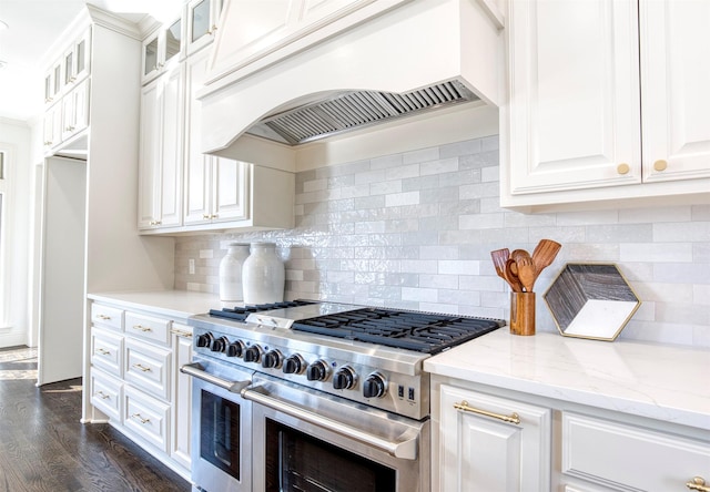 kitchen featuring light stone counters, white cabinets, glass insert cabinets, custom range hood, and range with two ovens