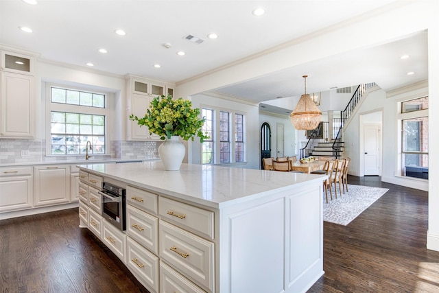 kitchen featuring recessed lighting, light stone counters, backsplash, a kitchen island, and ornamental molding