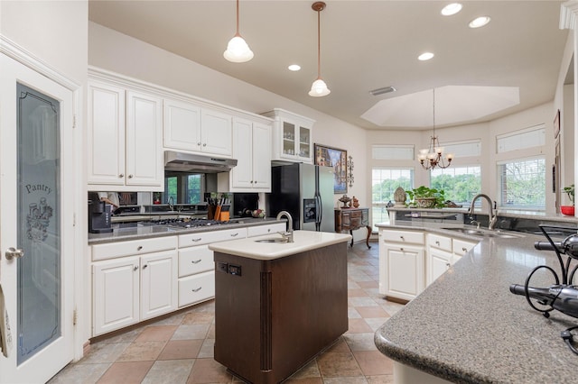 kitchen featuring under cabinet range hood, fridge with ice dispenser, a sink, a center island with sink, and a chandelier