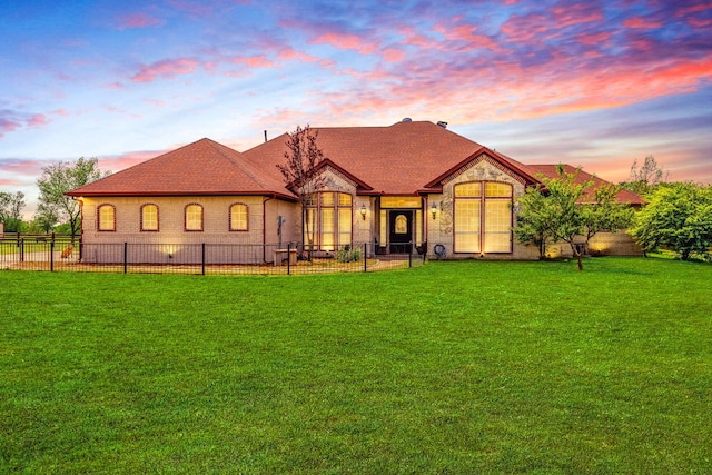 back of house featuring stone siding, fence, a yard, brick siding, and roof with shingles