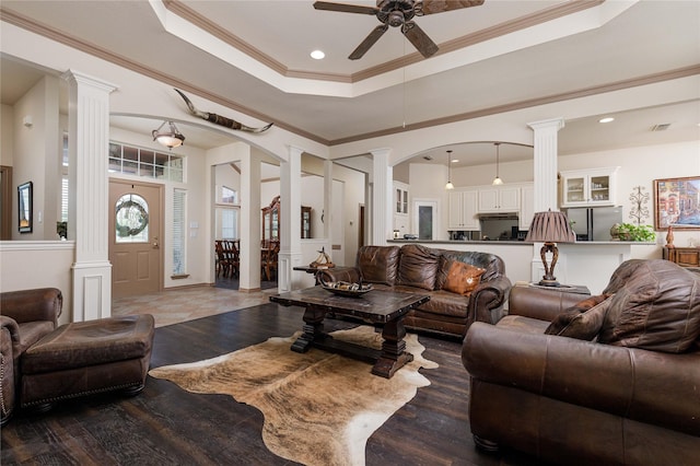 living room featuring ceiling fan, a raised ceiling, ornate columns, and crown molding