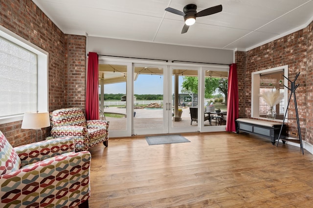 living area with wood finished floors, a ceiling fan, and brick wall