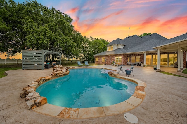 pool at dusk with fence, a patio area, and an outdoor pool