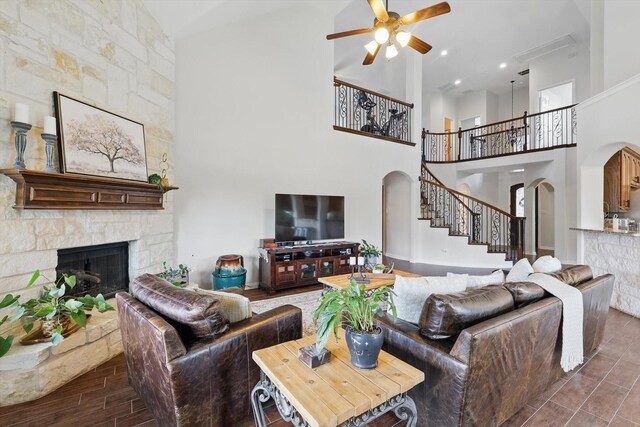 living room featuring high vaulted ceiling, stairway, a stone fireplace, ceiling fan, and arched walkways
