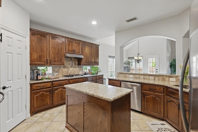 kitchen with arched walkways, tasteful backsplash, visible vents, under cabinet range hood, and appliances with stainless steel finishes