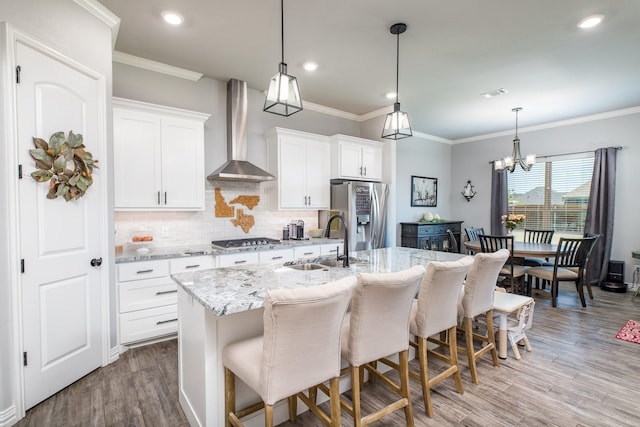 kitchen featuring a kitchen island with sink, a sink, visible vents, wall chimney range hood, and appliances with stainless steel finishes