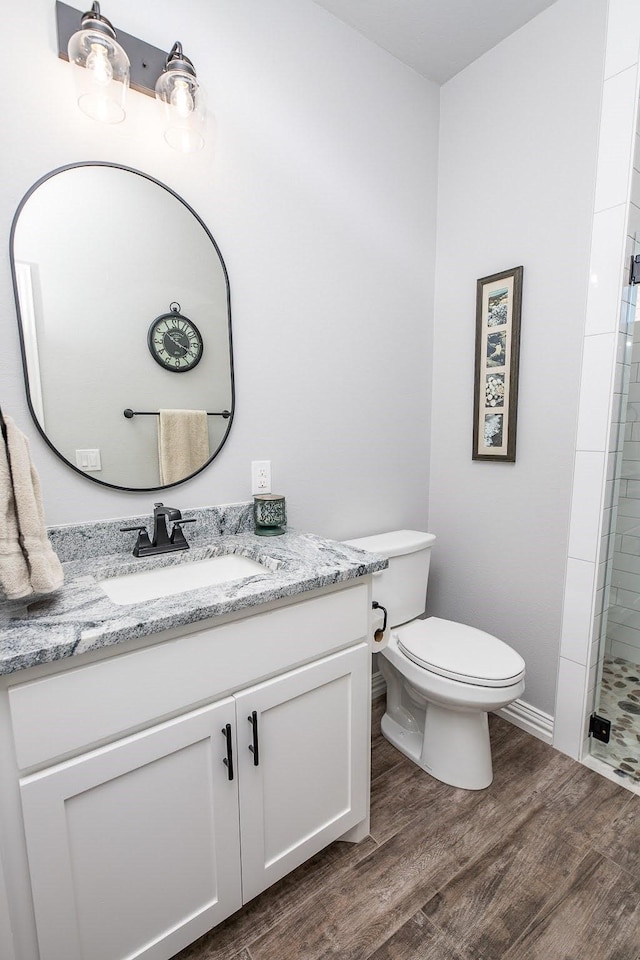 bathroom with tiled shower, wood finished floors, vanity, and toilet