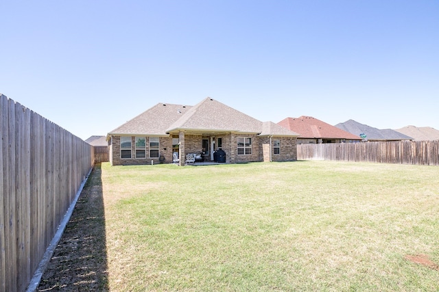 back of property with a fenced backyard, brick siding, and a yard