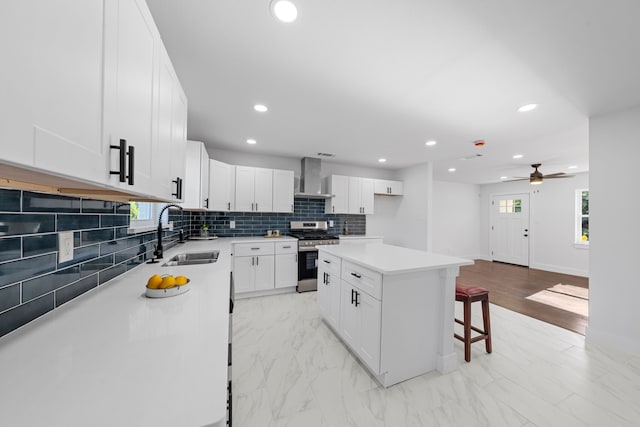 3712 Utah Ave, Dallas, TX 75216 - kitchen with stainless steel range with gas cooktop, a sink, ceiling fan, wall chimney range hood, and a breakfast bar area