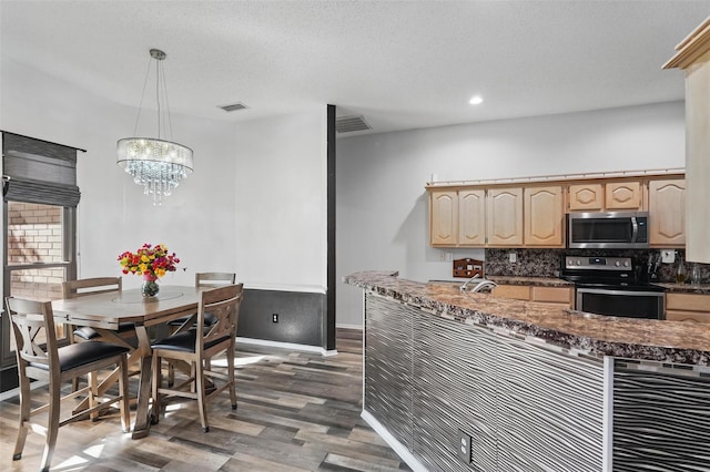 kitchen featuring dark countertops, visible vents, wood finished floors, light brown cabinets, and appliances with stainless steel finishes