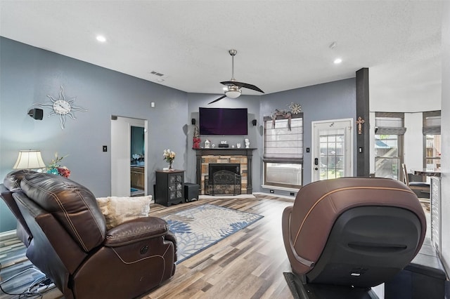 107 Princeton Cir, Forney, TX 75126 - living room featuring wood finished floors, a ceiling fan, recessed lighting, a stone fireplace, and a textured ceiling