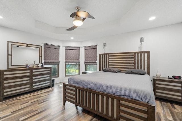 bedroom featuring ceiling fan, a tray ceiling, wood finished floors, and recessed lighting