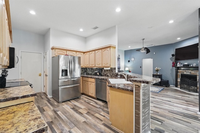 107 Princeton Cir, Forney, TX 75126 - kitchen with stainless steel appliances, a peninsula, light brown cabinets, a sink, and light wood-style flooring