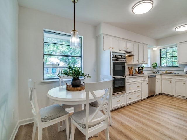 kitchen with dobule oven black, light wood finished floors, stainless steel dishwasher, and white cabinetry